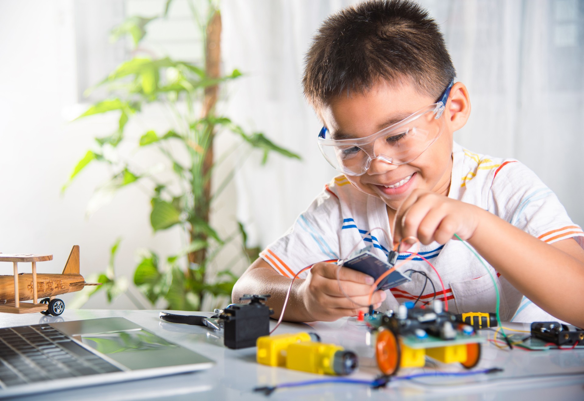 Asian kid boy plugging energy and signal cable to sensor chip with A.I. robot car