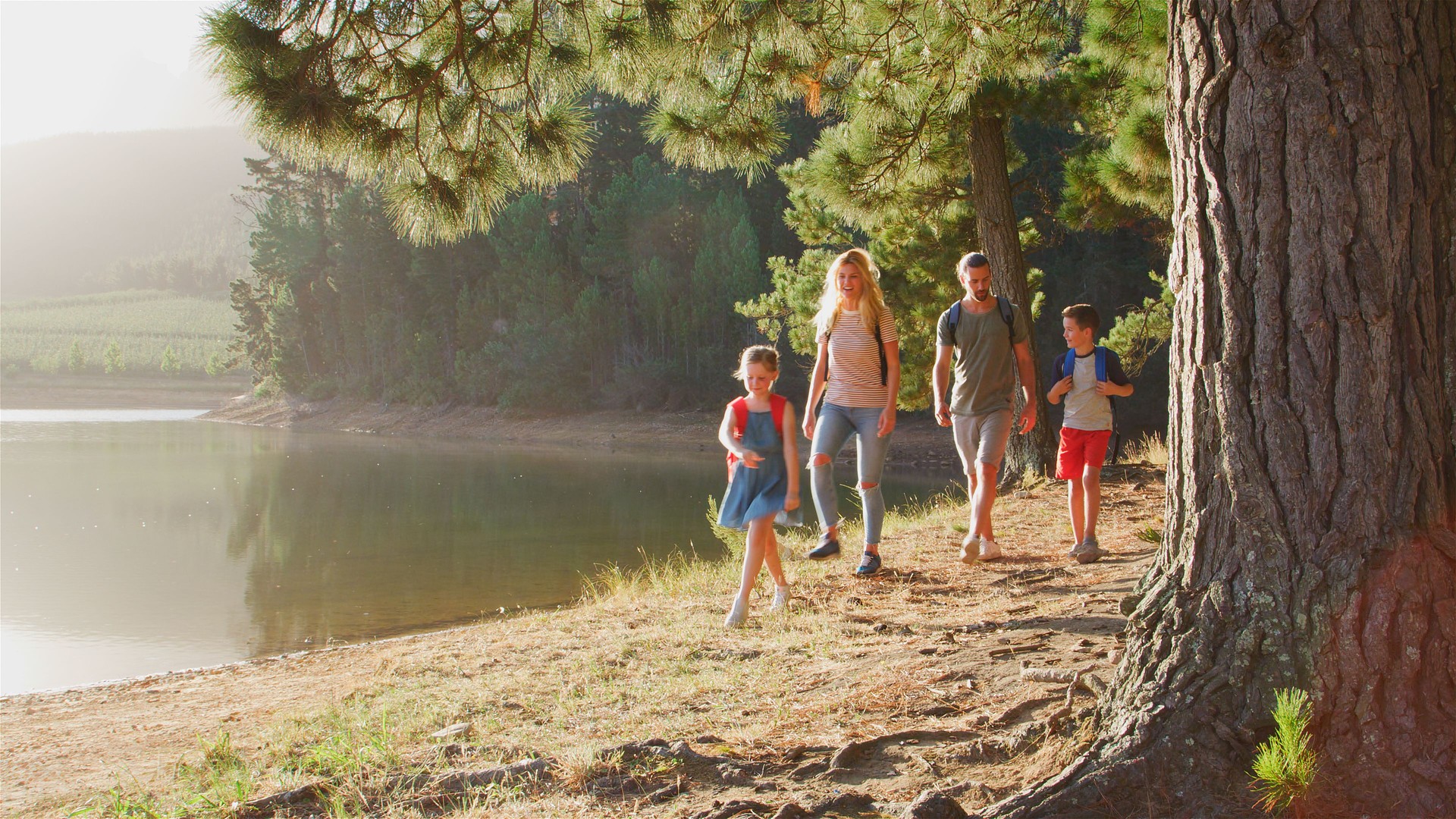 Family On Hiking Adventure Walking Along Path Through Woods By Lake