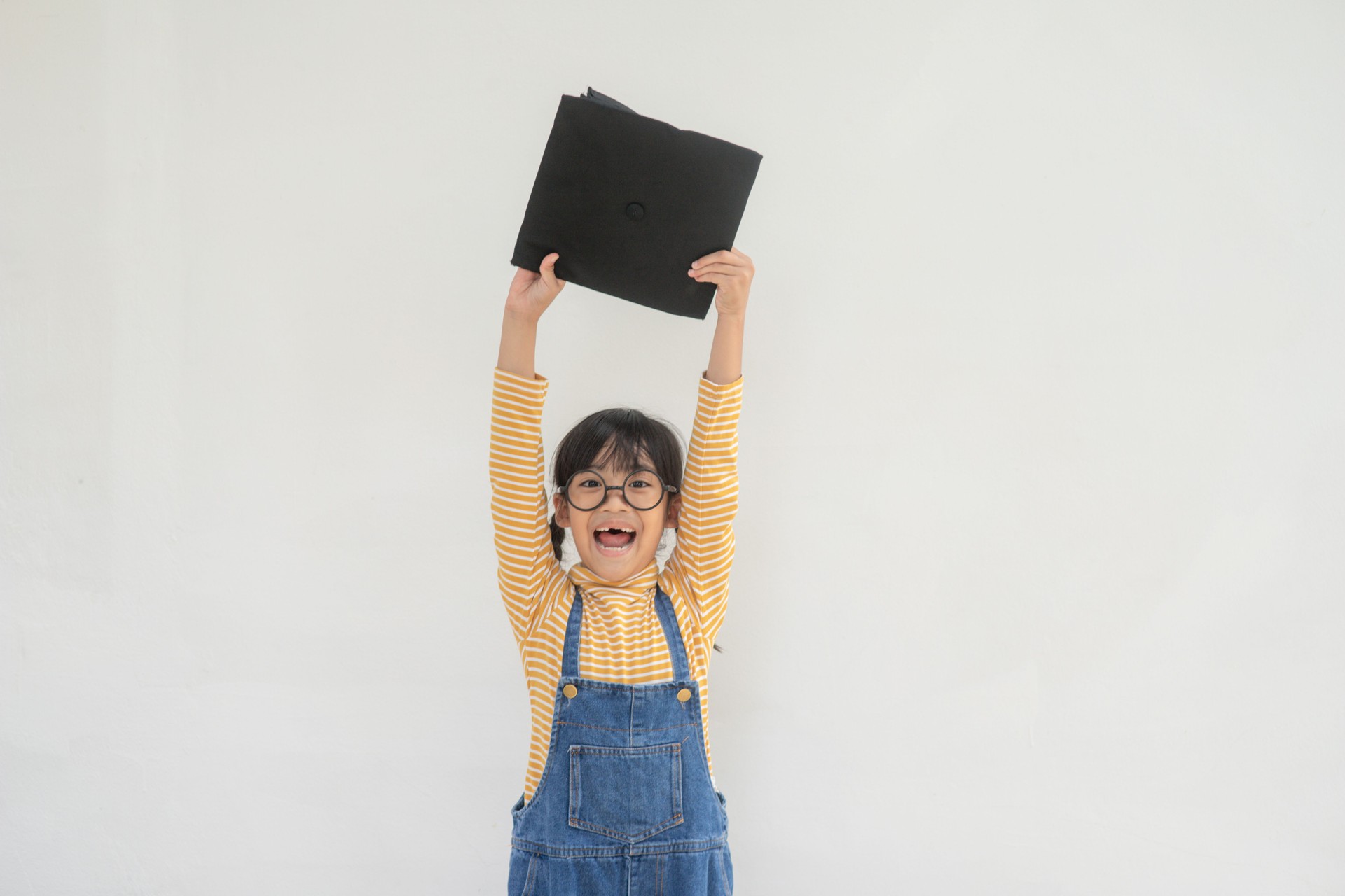 children girl wearing a graduate cap over white background very happy and excited doing winner gesture with arms raised, smiling and screaming for success. Celebration concept.