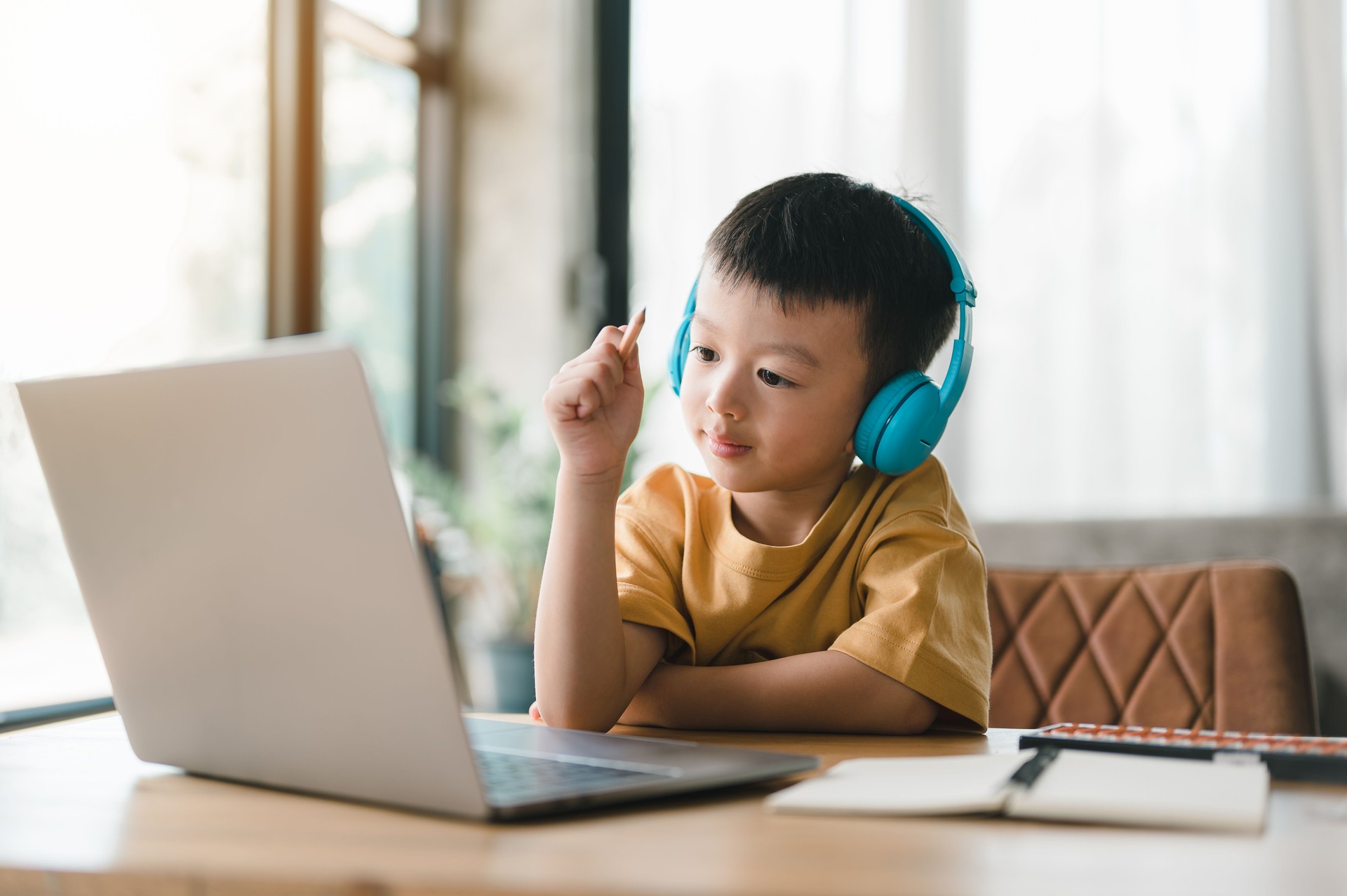 handsome cute Asian boy with looks at the camera while sitting and studying at home on a laptop to study from home during Covid-19 pandemic lockdown. Online education, Homeschooling.