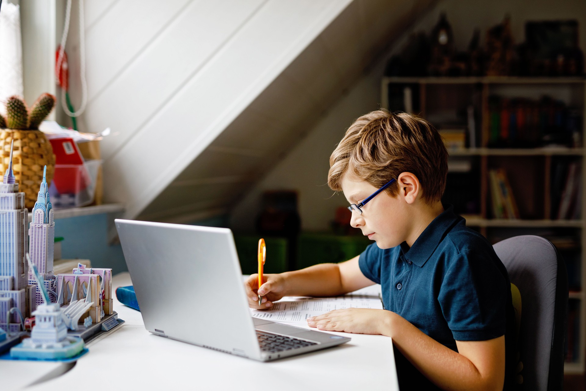 Kid boy with glasses learning at home on laptop for school. Adorable child making homework and using notebook and modern gadgets. Home schooling concept.