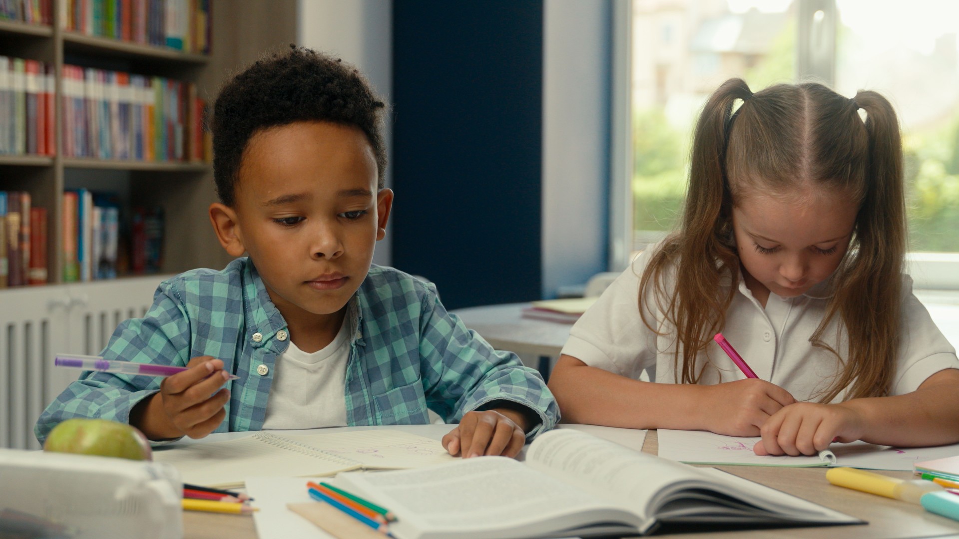African American schoolboy Caucasian schoolgirl little kids children multiracial concentrated girl boy pupils students studying together primary school education drawing writing homework exercise desk